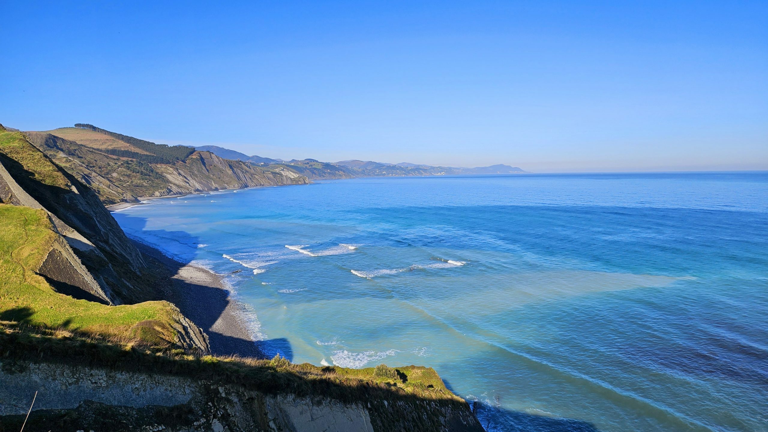 Vista panorámica del Flysch en la costa de Gipuzkoa, con acantilados verdes y aguas turquesas bajo un cielo despejado